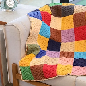 May include: A handmade crochet blanket featuring a patchwork design of square blocks in various colors including red, yellow, blue, green, brown, pink, and purple. The blanket has a textured stitch pattern and a light beige scalloped border edge.