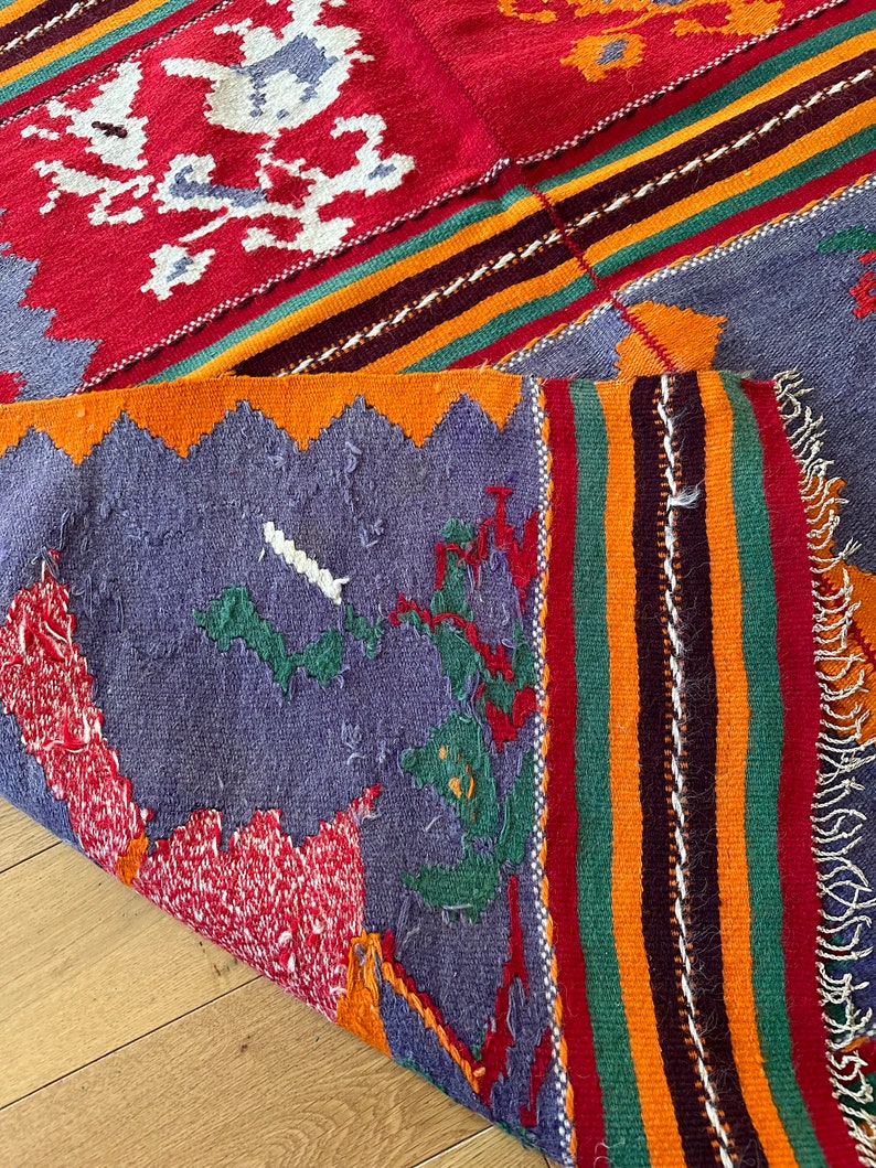 May include: A colorful woven rug with a geometric pattern in shades of red, orange, yellow, green, blue, and white. The rug has a fringed edge and is folded in half.