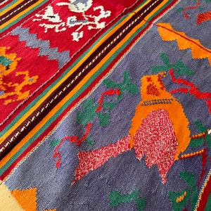 May include: A colorful woven rug with a geometric pattern in shades of red, orange, green, and blue. The rug features a bird design in the center.
