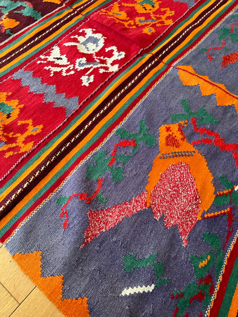 May include: A colorful woven rug with a geometric pattern in shades of red, orange, green, and blue. The rug features a bird design in the center.