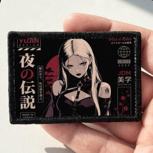 May include: A rectangular embroidered patch with a black border featuring an anime-style illustration of a person with long light hair in a dark outfit. The design includes red and white text, Japanese characters, a red circle, and cherry blossom graphics.
