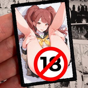 May include: A rectangular embroidered patch featuring a colorful anime-style illustration of a character with brown hair in pigtails, wearing a school uniform with a yellow bow. A red circular symbol with the number 18 is overlaid on the image.
