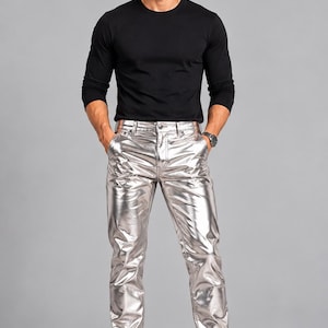 Könnte beinhalten: Ein langärmeliges schwarzes Shirt mit Rundhalsausschnitt kombiniert mit einer metallisch silbernen Hose. Die Hose verfügt über ein klassisches Fünf-Taschen-Design mit Knopf- und Reißverschluss. Das Outfit wird durch schwarze Sneaker mit weißen Sohlen ergänzt.