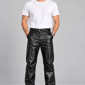 Puede incluir: Una camiseta blanca lisa de manga corta y cuello redondo combinada con pantalones de cuero negro con cintura estándar, trabillas para cinturón, cremallera frontal y un cinturón de cuero negro con hebilla de metal plateado, usados con zapatos negros.