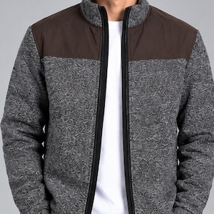 May include: A zip-up jacket featuring a textured charcoal gray knit body with solid dark brown panels on the upper chest and shoulders. The jacket has a high collar, a black front zipper, and long sleeves with ribbed cuffs, worn over a plain white t-shirt.