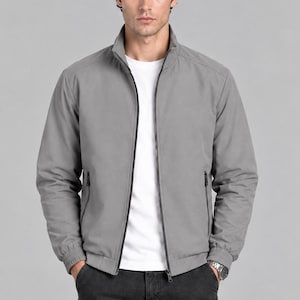 May include: A light gray zip-up jacket with a stand-up collar, long sleeves with ribbed cuffs, and two side pockets with black zippers. The jacket is worn over a plain white t-shirt and paired with dark gray cargo pants featuring side pockets.