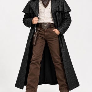 May include: A black long duster coat worn over a beige button-down shirt, brown jeans, and a brown leather belt with a large silver bull skull buckle. A dark brown patterned bandana is tied around the neck, and a brown leather holster is attached.