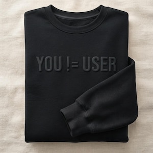 May include: A black long-sleeve sweatshirt featuring the text YOU != USER embossed in a tonal black finish across the chest. The garment has a ribbed crew neckline and ribbed cuffs on the sleeves, presented in a folded, flat layout.