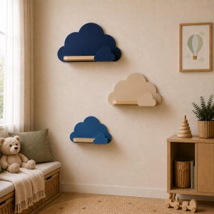 Puede incluir: Tres estantes de pared con forma de nube. Dos estantes son de color azul marino oscuro con una repisa de madera clara, y un estante es de color beige claro con una repisa de madera clara a juego. Cada estante tiene un pequeño adorno de nube.