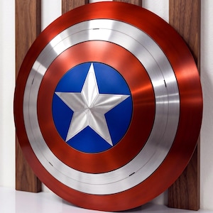 May include: A circular shield featuring a metallic red outer ring, a silver middle ring, and a central blue circle containing a large, five-pointed silver star. The design is symmetrical with a smooth, polished finish across the entire surface.