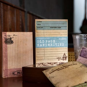 Puede incluir: Una colección de papelería de estilo vintage que incluye una tarjeta de biblioteca con una banda azul etiquetada OLD PAGE HANDWRITING, una hoja cuadriculada con texto escrito a mano y una tarjeta color canela con el texto FABRIQUE DE CHOCOLATS.