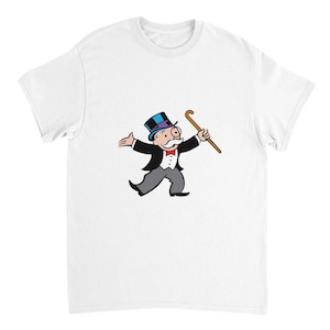 Op de afbeelding: Een wit t-shirt met korte mouwen en een afbeelding van een stripfiguur met een blauwe hoge hoed, een zwarte pandjesjas, een wit vest, een rode vlinderdas en een grijze broek, terwijl deze een bruine wandelstok vasthoudt.