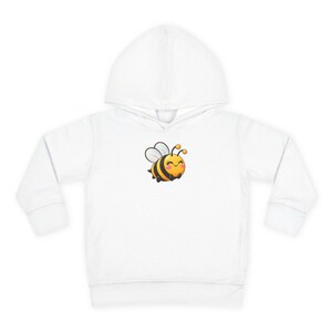 May include: A white long-sleeve hooded sweatshirt featuring a centred graphic of a small, round, yellow and black striped bee with white wings, pink cheeks, and a smiling expression. The hoodie has a front pouch pocket and a hood.
