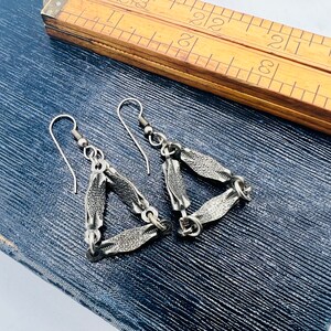 May include: A pair of silver triangle earrings with a textured finish. The earrings are made of linked chains with a triangular shape.