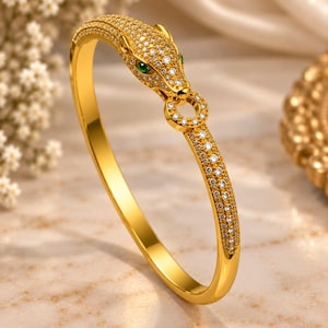 Può includere: Un bracciale rigido color oro caratterizzato da un motivo a testa di pantera stilizzata su un'estremità. La testa della pantera e il bracciale sono incastonati con numerose piccole pietre chiare e scintillanti. La pantera ha due occhi verde vivo.