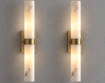 May include: A pair of wall sconces featuring cylindrical white marble shades with grey veining. Each light fixture is mounted on a rectangular brass backplate and includes a central horizontal brass band separating the two marble segments.