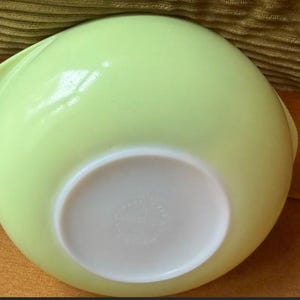 May include: A light lime green mixing bowl with a smooth, glossy finish and a rounded shape. The base of the bowl is white and features embossed text that reads Made in USA, along with a number, indicating its origin and manufacturing details.