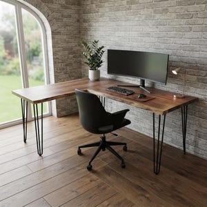 May include: An L-shaped desk with a natural live edge wood top and black metal hairpin legs. The desk holds a curved computer monitor, a keyboard, a mouse on a pad, a small potted plant, and a desk lamp. A black office chair with wheels sits in front.