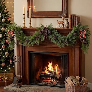May include: A green pine garland decorated with brown pinecones and red and gold striped bows draped across a wooden fireplace mantel. The mantel features two brass candlesticks, a deer figurine, an owl figurine, and four books.