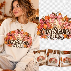 Pode incluir: Uma camisola cor de creme com um gráfico de três abóboras adornadas com laços cor-de-rosa axadrezados e laços cor-de-rosa sólidos, rodeadas por folhas de outono e bolotas, com o texto COZY SEASON CLUB numa fonte decorativa castanha.