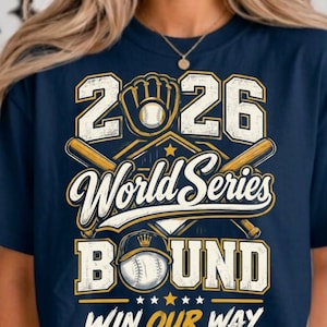 May include: A navy blue t-shirt featuring a graphic design with the text 2026 World Series Bound Win Our Way. The print includes a baseball glove, two crossed wooden bats, and two baseballs in white, yellow, and navy blue colors.