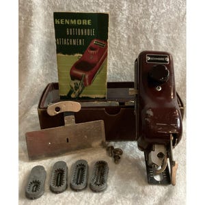 May include: A vintage Kenmore buttonhole attachment set including a dark brown metal sewing machine accessory, a metal plate, four grey plastic cams, two small screws, and an instruction manual titled Kenmore Buttonhole Attachment.