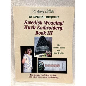 May include: A softcover instructional book titled Avery Hill's By Special Request Swedish Weaving/Huck Embroidery, Book III by Jeanne Tams and Nan Duffin. The cover features three photographs showing a person wearing a vest, a black fabric piece, and a white fabric runner with embroidery patterns, all designed for monk's cloth and huck fabric.
