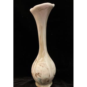 May include: A tall, slender glass vase featuring a swirling marbled pattern of cream, beige, and soft brown tones. The vessel has a bulbous base that tapers into a long, narrow neck, culminating in a wide, flared, and slightly ruffled rim.
