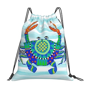 May include: A drawstring backpack featuring a vibrant, stylized crab illustration on a light blue and white wavy background. The crab has a blue body with geometric patterns, orange claws, and multiple legs, secured by black cord shoulder straps.