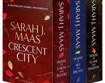 Peut inclure: Un coffret de trois livres intitulé Crescent City par Sarah J. Maas. La boîte présente un fond rouge profond avec des illustrations de feuilles dorées. Les tranches incluent House of Earth and Blood, House of Sky and Breath et House of Flame and Shadow.