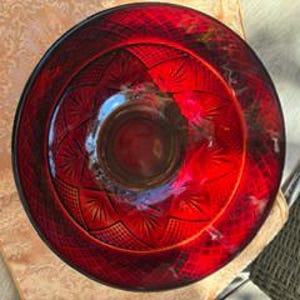 May include: A circular ruby red glass bowl featuring a pressed pattern of radiating fan shapes and cross-hatched diamond textures. The bowl has a smooth, thick rim and a deep, rounded interior, showcasing a vibrant, translucent crimson hue.