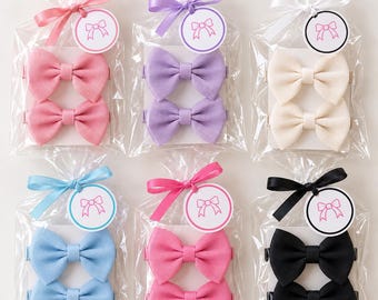May include: Six clear plastic bags, each containing two grosgrain ribbon hair bows on a white card. The colors are pink, lavender, cream, light blue, hot pink, and black. Each bag is tied with a matching ribbon and a circular tag with a bow icon.