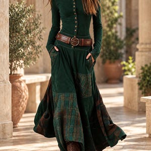 May include: A long-sleeved dark green dress with a button-down bodice, a brown leather belt with a circular buckle, and a full-length skirt featuring contrasting dark green fabric and green and brown plaid panels with side pockets.