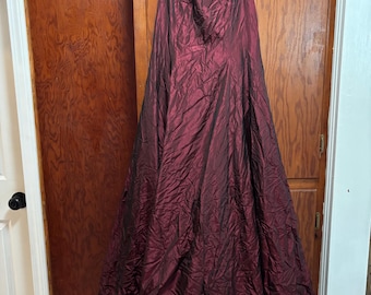 May include: A floor-length sleeveless dress in a deep burgundy color with a subtle iridescent sheen. The fabric features a crinkled, textured finish throughout the bodice and the full, flowing skirt, which hangs from a white plastic hanger.