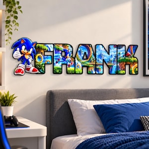 May include: A wall-mounted decorative sign spelling the name FRANK, featuring a graphic print of the character Sonic the Hedgehog and various game landscapes within each letter, with a black outline surrounding the entire name.