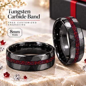 Puede incluir: Dos anillos de carburo de tungsteno de 8 mm de ancho, con un acabado negro martillado y una incrustación central de ópalo rojo triturado. El interior de cada anillo está grabado con el texto Tungsten Carbide, visible en la imagen.