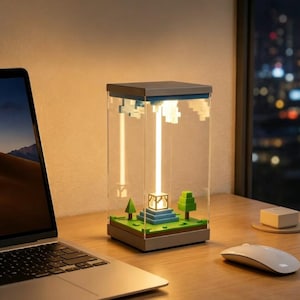 Op de afbeelding: Een rechthoekige, doorzichtige acryl vitrine met een pixelachtig miniatuurlandschap met een centraal oplichtend baken, groene bomen en een blauwe getrapte basis. De lamp straalt een heldere verticale lichtbundel uit naar witte wolken.