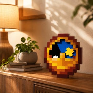 May include: A circular pixel-art style wall clock or decorative object featuring a brown outer frame, a bright yellow lower section, a deep blue background, a black cutout area, a small white square, and a prominent yellow cross-shaped element.