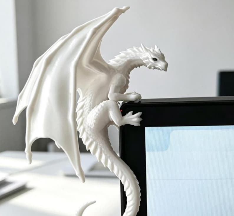 Pode incluir: Uma estatueta de drag&atilde;o branco com escamas detalhadas, asas grandes e uma cauda longa, projetada para pousar no canto superior de um monitor de computador. A criatura tem uma cabe&ccedil;a angular e garras que agarram a moldura preta da tela.