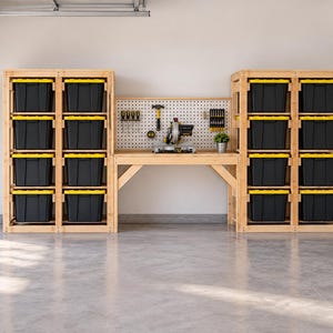 Puede incluir: Un banco de trabajo de madera con un panel perforado blanco, flanqueado por dos estanterías altas de madera. Cada unidad contiene cuatro cajas de almacenamiento de plástico negro con tapas amarillas. Una sierra ingletadora y herramientas están colgadas.