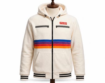 May include: A cream-colored zip-up hoodie featuring a horizontal stripe pattern in blue, purple, red, and orange across the chest. The garment includes a black front zipper, two zippered chest pockets, and black and white striped ribbed cuffs and hem.