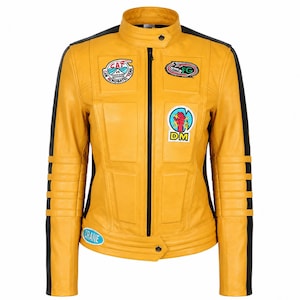 May include: A yellow leather jacket with black side panels and a stand-up collar. The jacket features a central black zipper, ribbed detailing on the sleeves, and various colorful patches including text reading CAT, FG, DM, and CRANE.