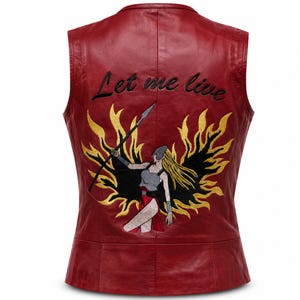 Può includere: Un gilet senza maniche in pelle rossa con un ricamo sul retro. Il ricamo raffigura una figura con lunghi capelli biondi che tiene una lancia, circondata da fiamme nere e gialle. Il testo Let me live è ricamato in filo nero.