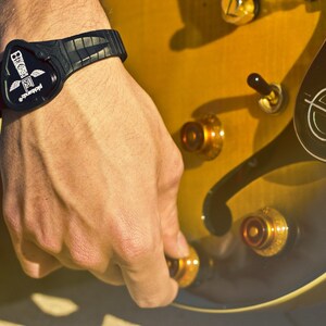 May include: A black wristband with a white logo that says "Guitarist" and a graphic of a guitar pick. The wristband is worn on a person's wrist.