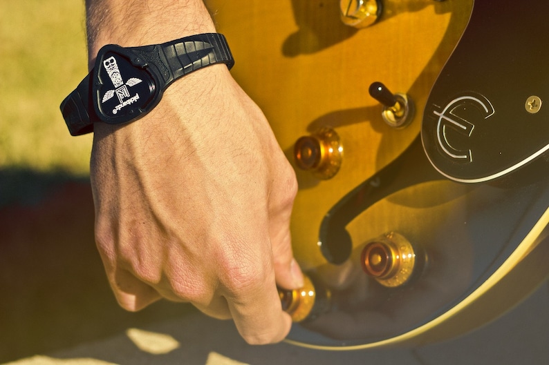 May include: A black wristband with a white logo that says "Guitarist" and a graphic of a guitar pick. The wristband is worn on a person's wrist.