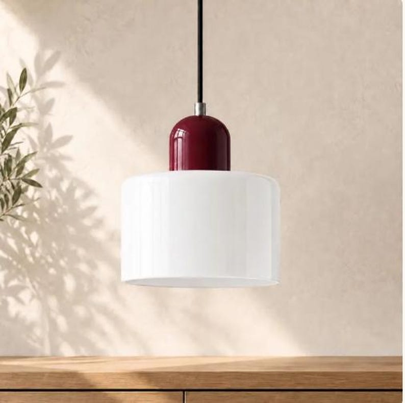 May include: A pendant light fitting featuring a cylindrical white glass shade suspended by a black cord. The top of the shade is accented with a glossy, deep burgundy dome-shaped cap that connects to the cord with a silver-toned metal fitting.
