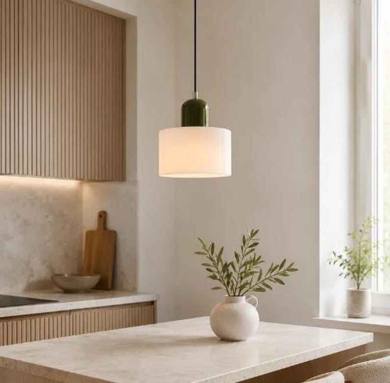 May include: A pendant light fitting featuring a cylindrical white frosted glass shade suspended by a black cord, topped with a smooth olive green cap. The light hangs vertically, providing a clean, focused illumination source.