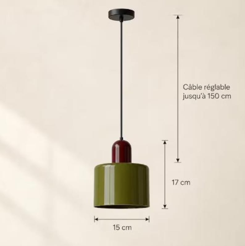 May include: A pendant light with a cylindrical olive green shade, a dark red top cap, and a black cord. The fixture has a height of 17 cm and a diameter of 15 cm. The cord is adjustable up to 150 cm as indicated by the text in the image.