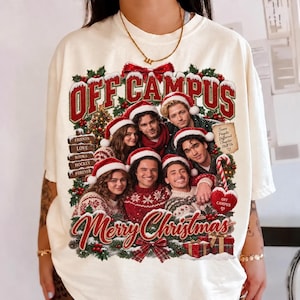 Puede incluir: Una camiseta color hueso con un estampado gráfico de cinco personas con gorros de Papá Noel. El texto dice OFF CAMPUS y Merry Christmas, con un letrero que enumera FRIENDS, LOVE, BOOKS, HOCKEY, FOREVER. Un adorno en forma de corazón dice OFF CAMPUS.