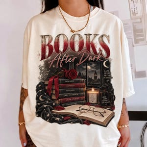 Może przedstawiać: Kremowy t-shirt z nadrukiem graficznym z napisem "BOOKS After Dark". Wzór przedstawia stos książek z etykietami Romance, Fantasy, Mystery, Dark Academia, Good Stories i Happier Me, czerwoną różę, świecę oraz okulary.